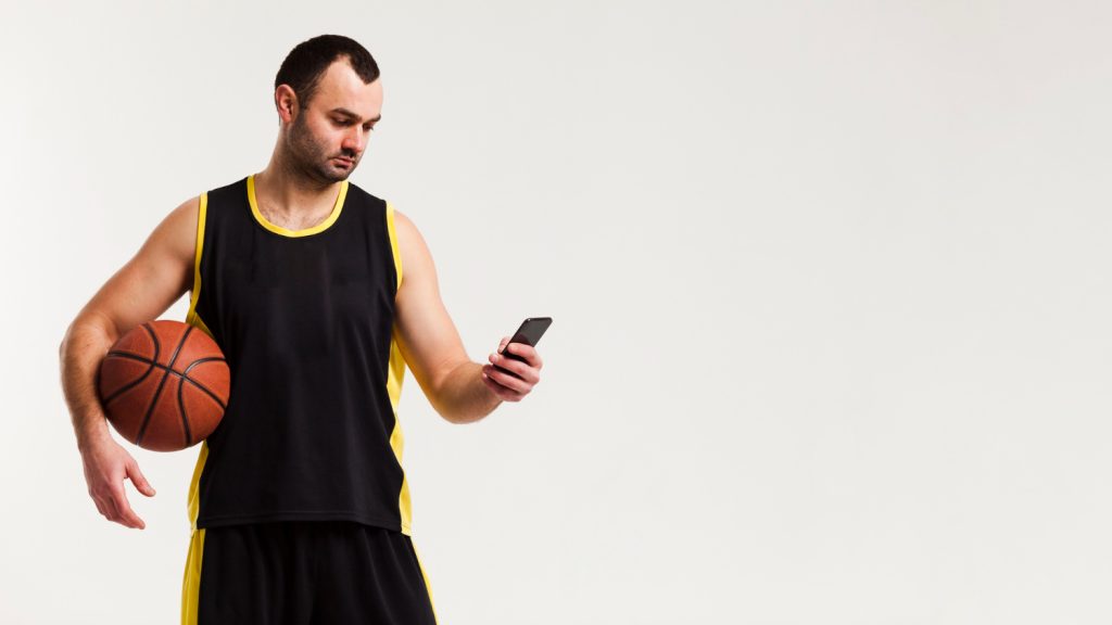 Homem com bola de basquete e celular em fundo branco - Foto: Freepik